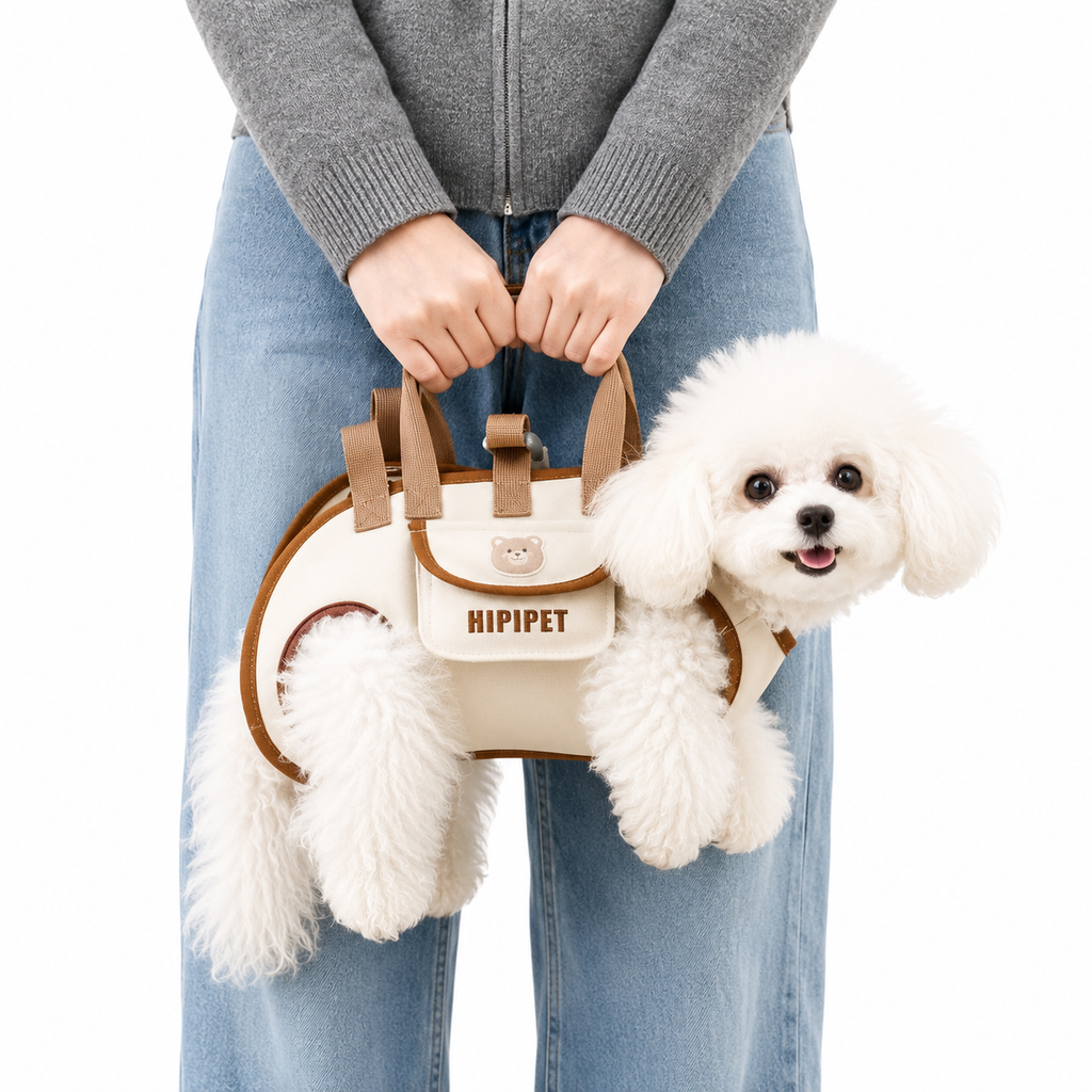 A small white fluffy dog sits inside a cream and brown pet carrier bag held by a person wearing a gray zip-up sweater and blue jeans against a white background.